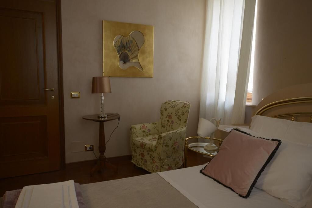A hotel room with a bed, a chair, a table, a lamp, and a painting on the wall.