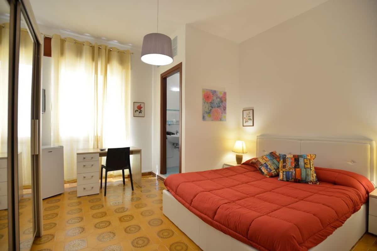 Un dormitorio con cama, escritorio, silla, lámpara y espejo.