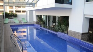 A swimming pool with a tiled deck, lounge chairs, and a glass-enclosed upper level. - Premium Residence The Currency Ortigas (Pasig)