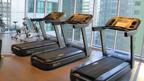 Three treadmills in a gym with large windows and a view of buildings. - Premium Residence The Currency Ortigas (Pasig)