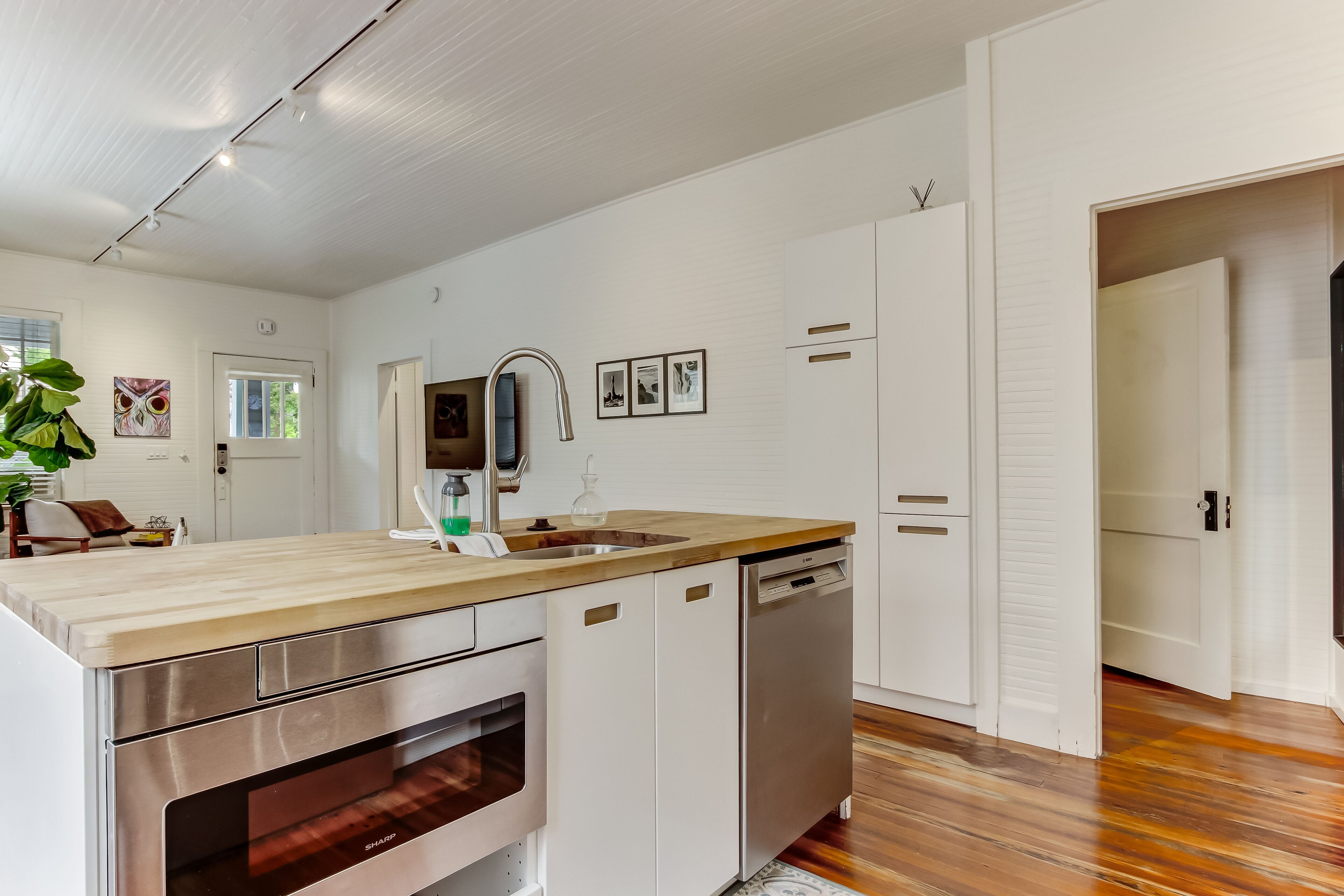 A modern kitchen with white cabinetry, a wooden countertop, a built-in oven, and a dishwasher.