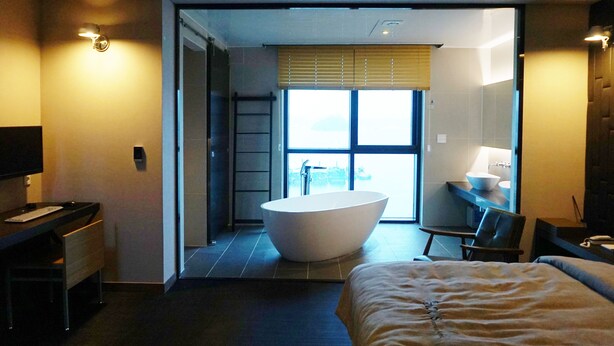 A modern hotel room with a large bathtub, a desk, a chair, and a bed. - Louis Boutique Hotel (Changwon)