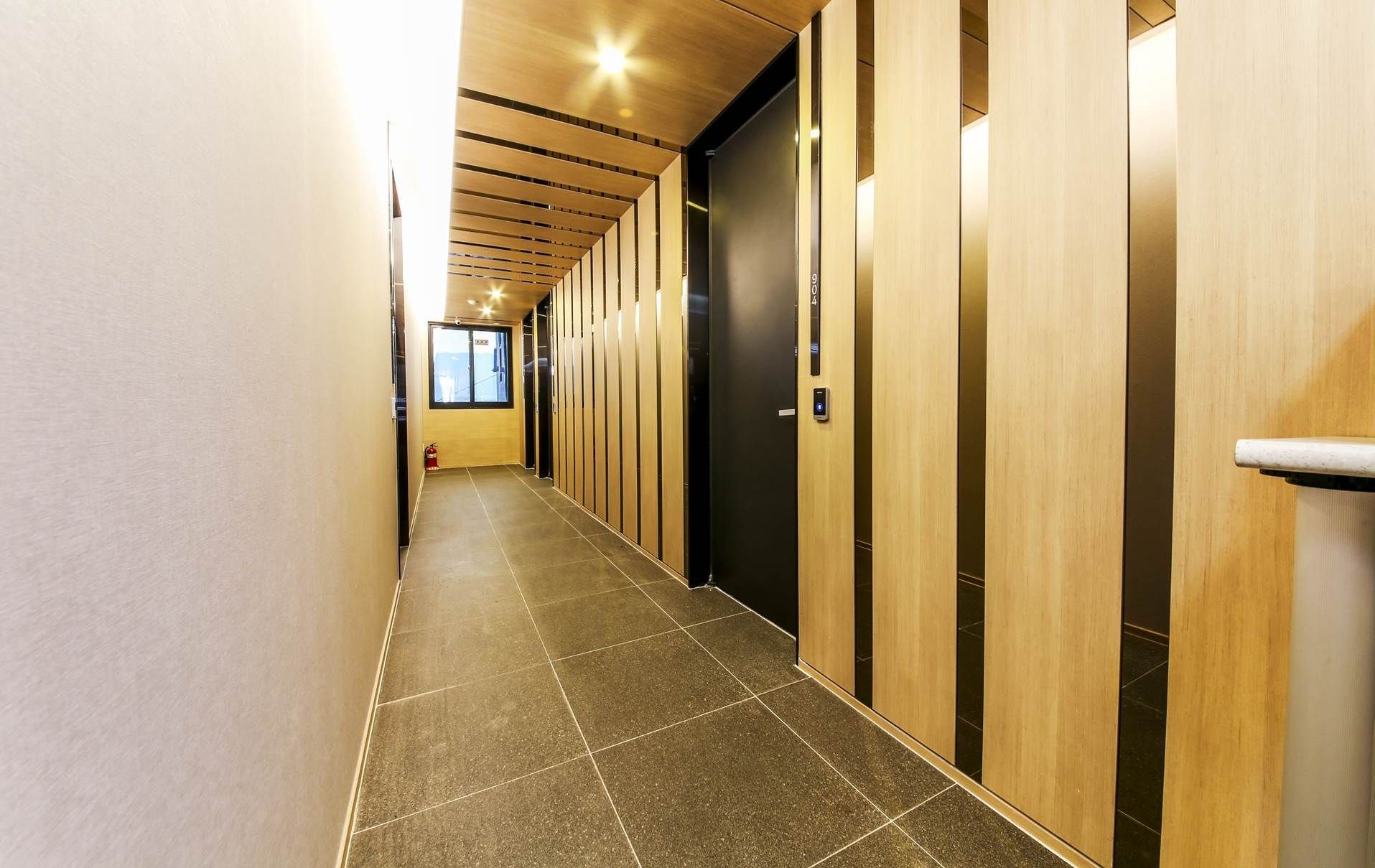 A hallway with a tiled floor, wooden paneling on the walls, and a series of elevators.