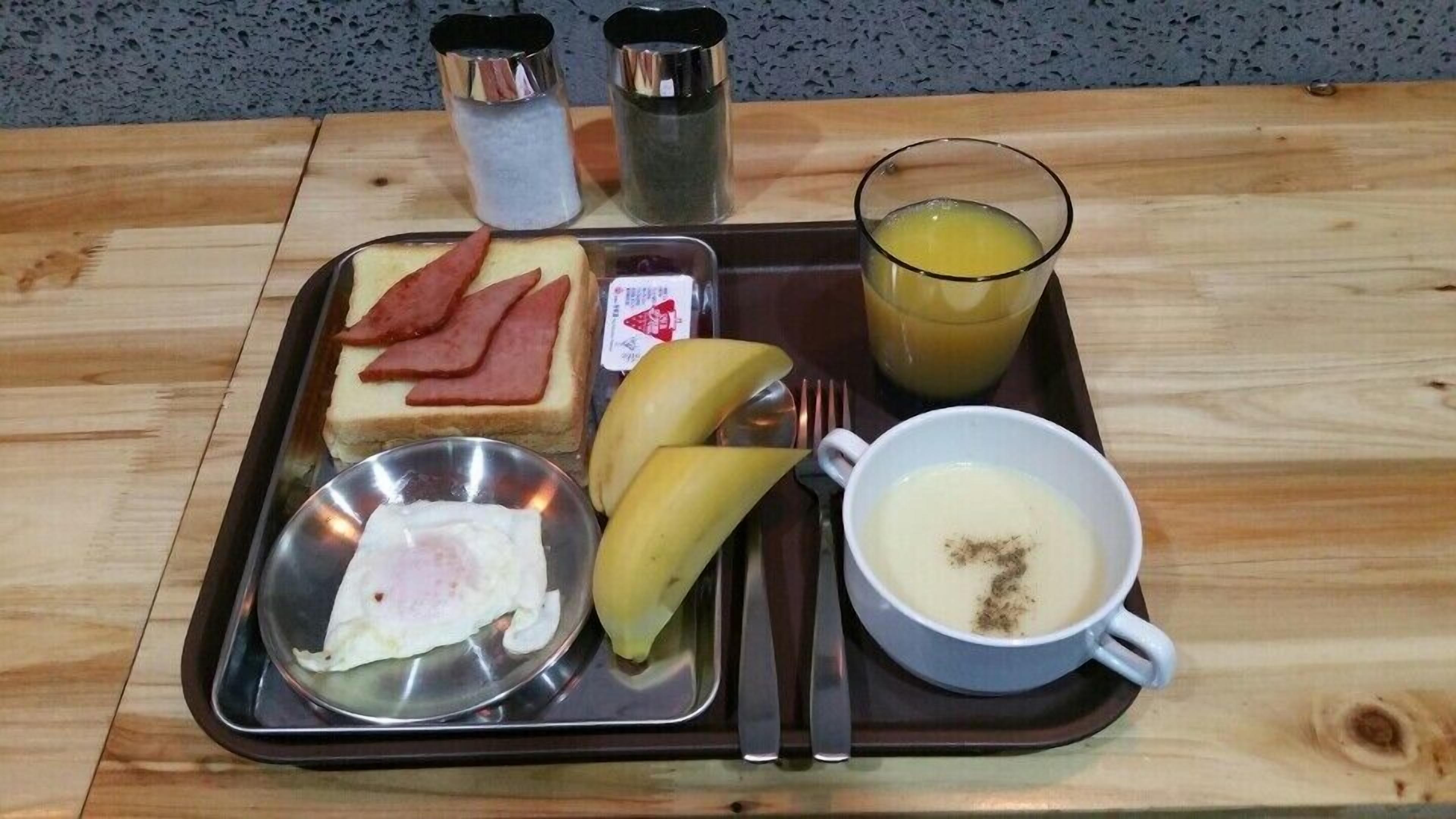 A tray with breakfast items including toast, ham, eggs, bananas, and a cup of coffee.
