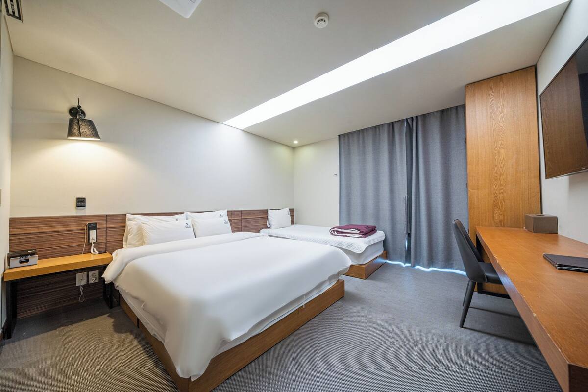 A hotel room with two beds, a desk, a chair, a TV, and a window with curtains.