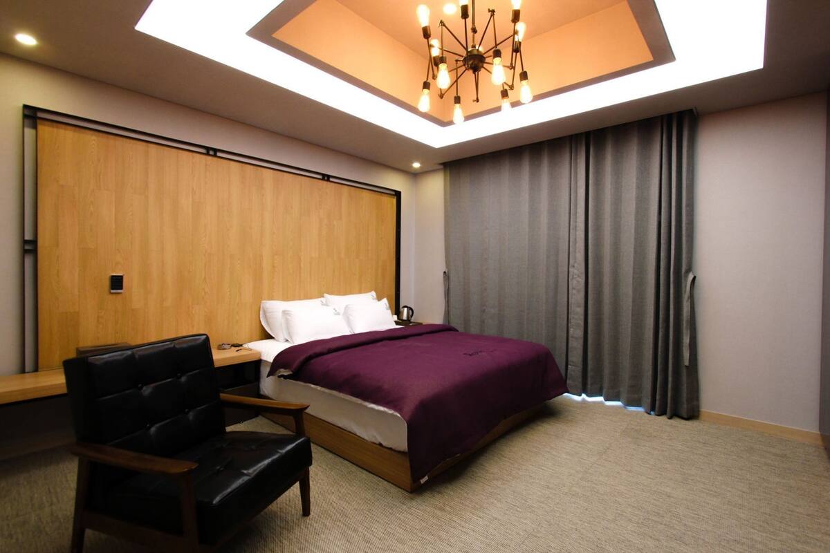 A hotel room with a skylight, a bed, a desk, a chair, and a large window with curtains.