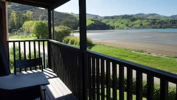Terraza de madera con una mesa y sillas, con vista a un río y colinas.