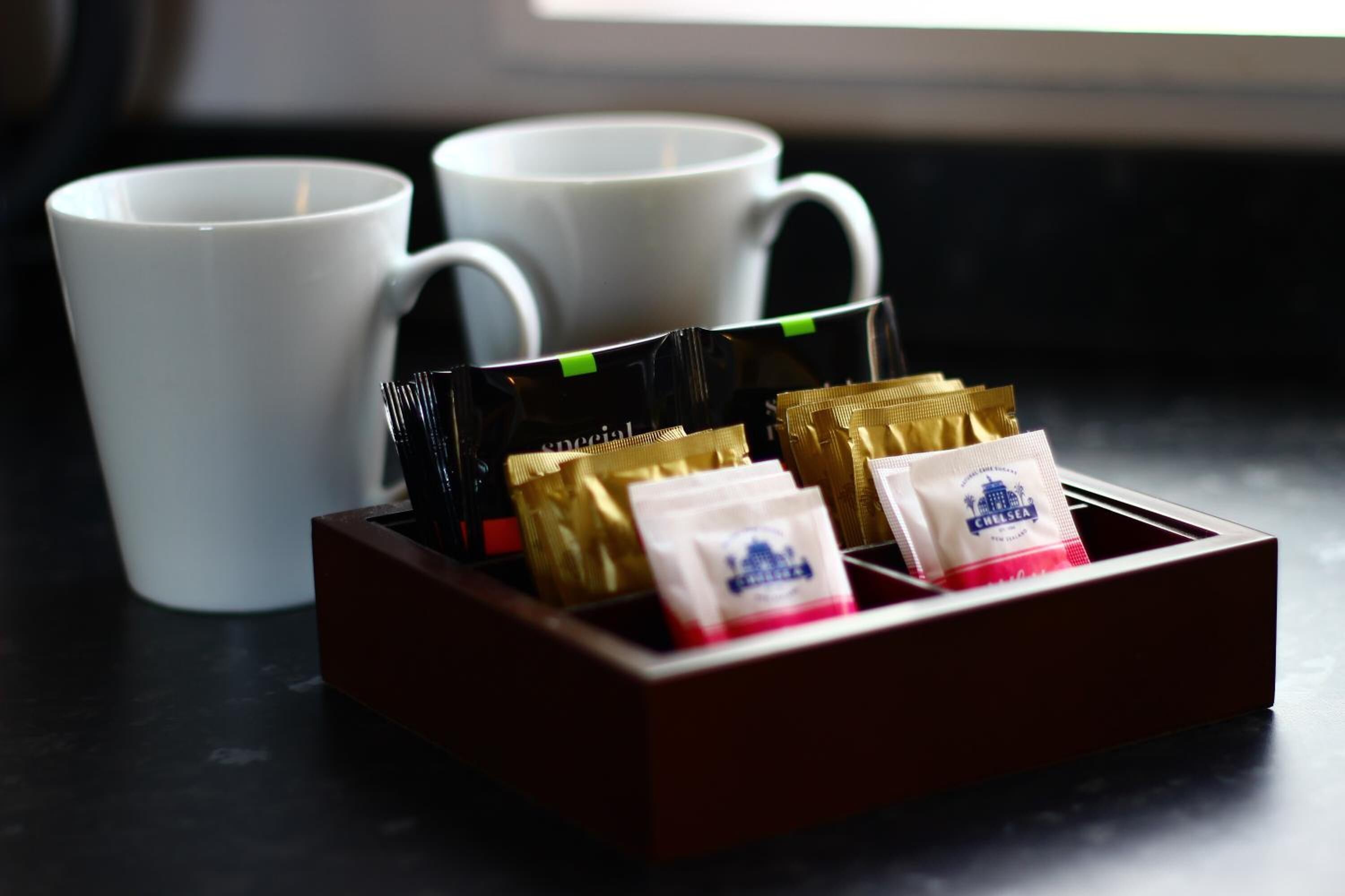 Una bandeja con sobres de café y dos tazas blancas sobre una superficie oscura.