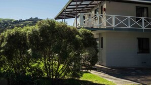 A two-story building with a balcony, surrounded by greenery and hills in the background.