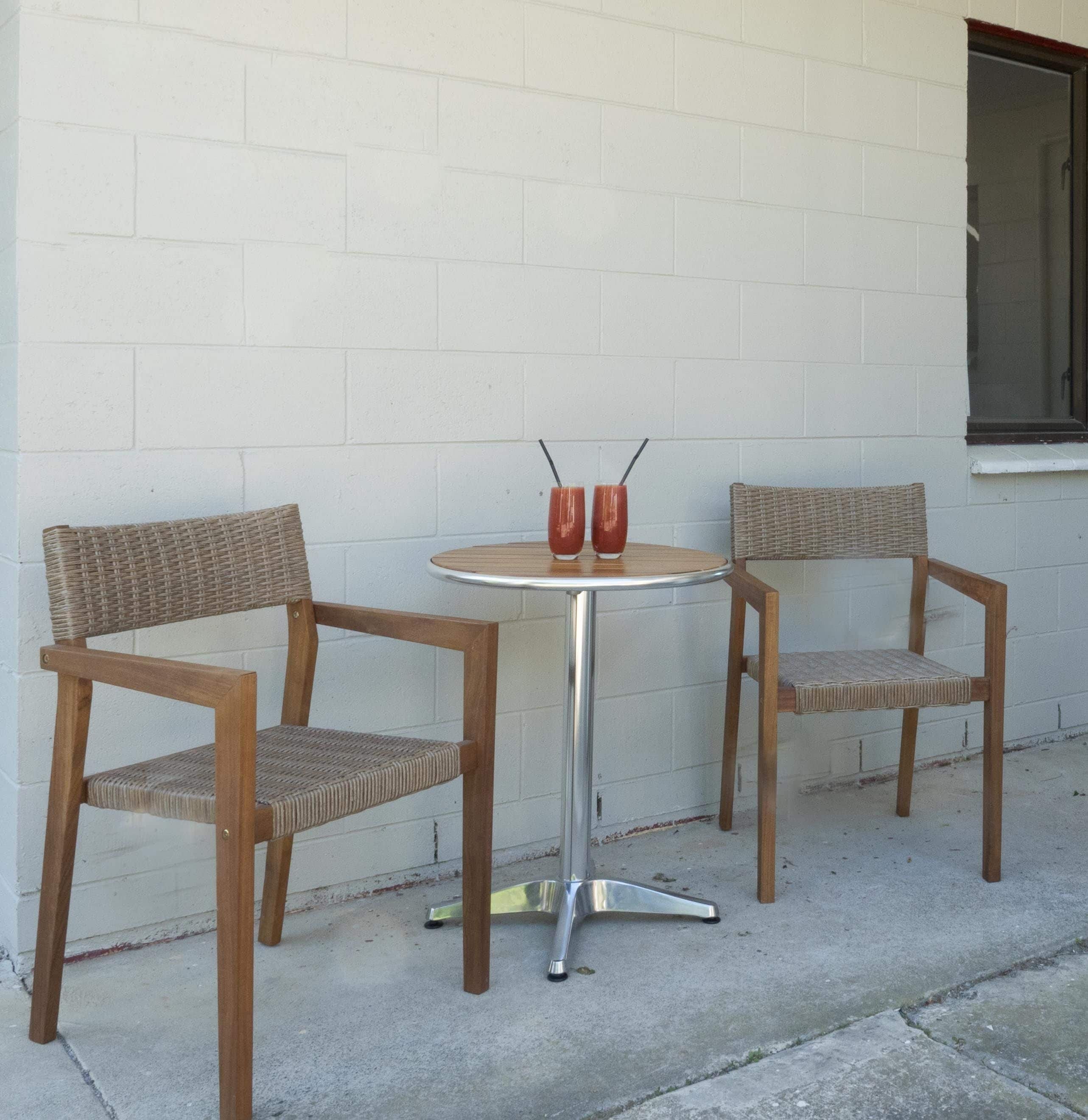 A small outdoor seating area with two wicker chairs and a round table, featuring two red glasses with straws.