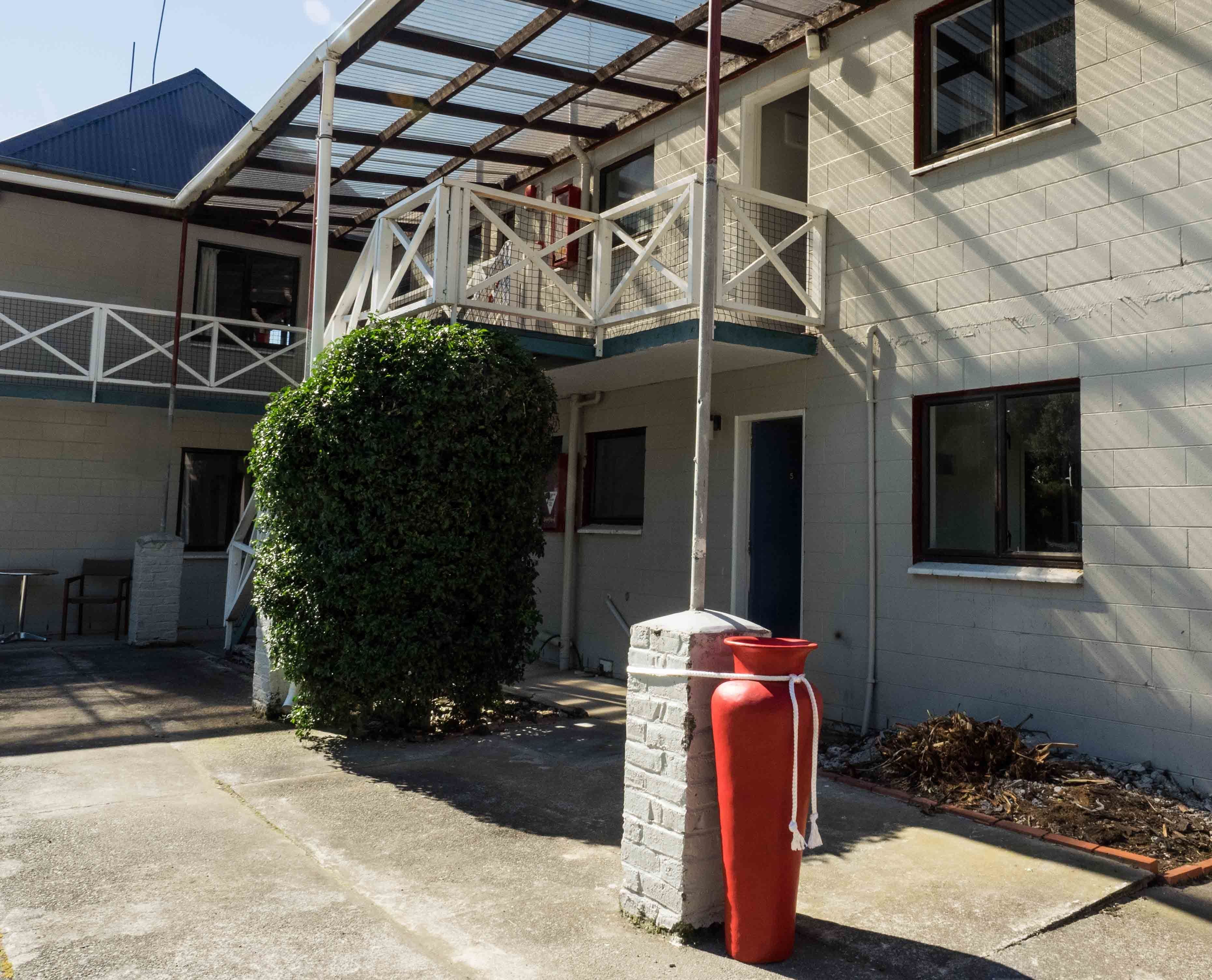 A building with a covered patio area, a large green bush, and a red mailbox.