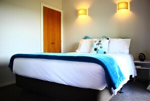 A bed with a blue blanket, white pillows, and a wooden door.