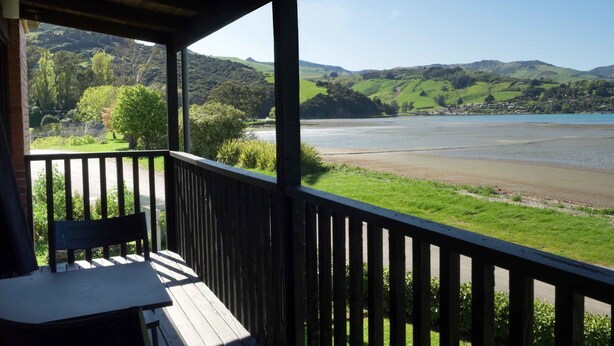 A wooden deck with a table and chairs, overlooking a river and green hills.