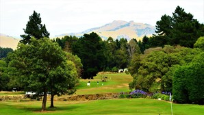 A golf course with a flagstick, trees, and distant mountains.