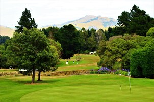Um campo de golfe com mastro de sinalização, árvores e montanhas ao longe.
