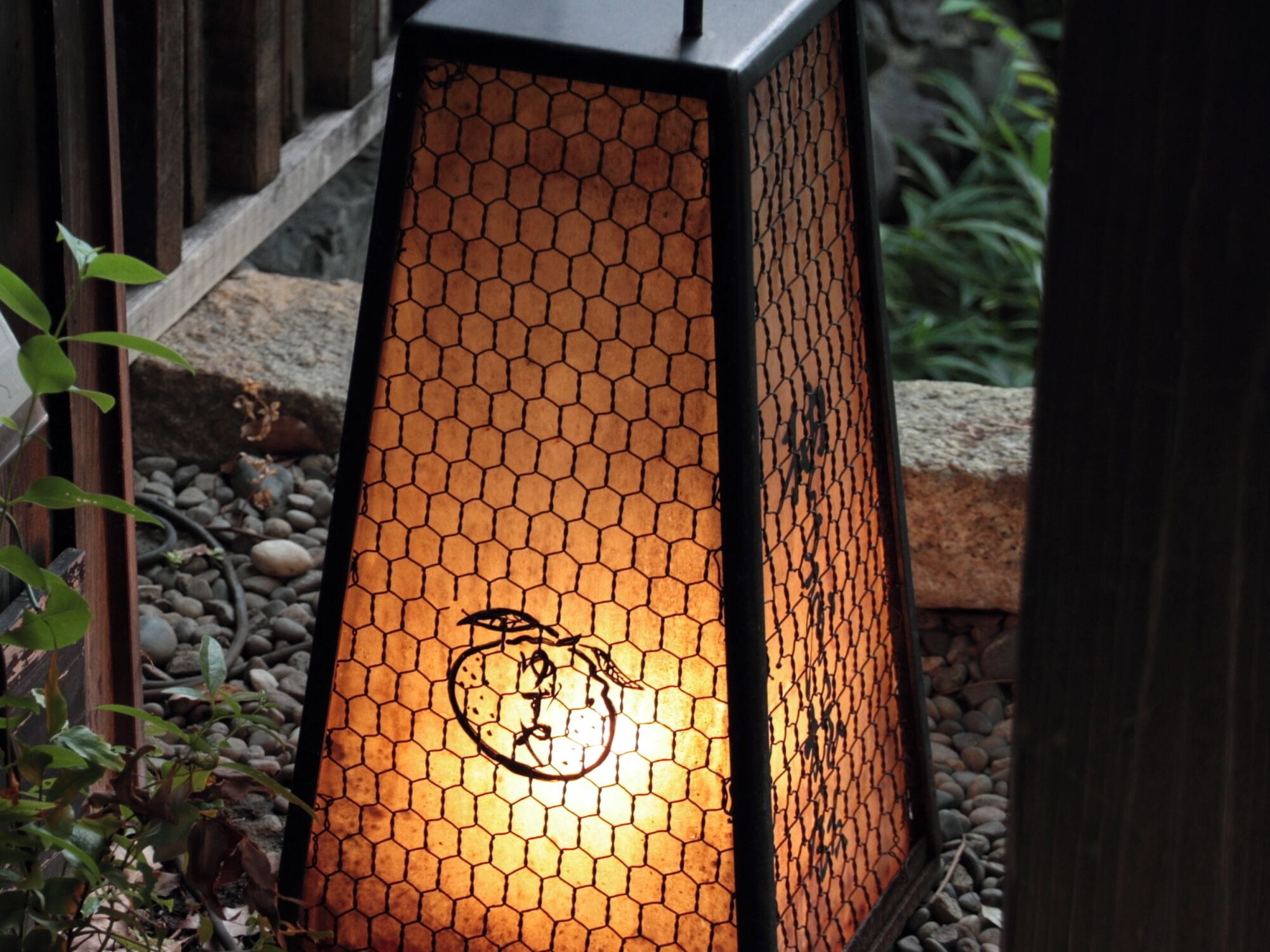 A hexagonal lantern with a honeycomb pattern, placed outdoors on a gravel surface.