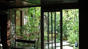 A room with a wooden bench, a window with vertical blinds, and a view of a garden with a stone path. - Yuzuya Ryokan - Adult Only (Kyoto)