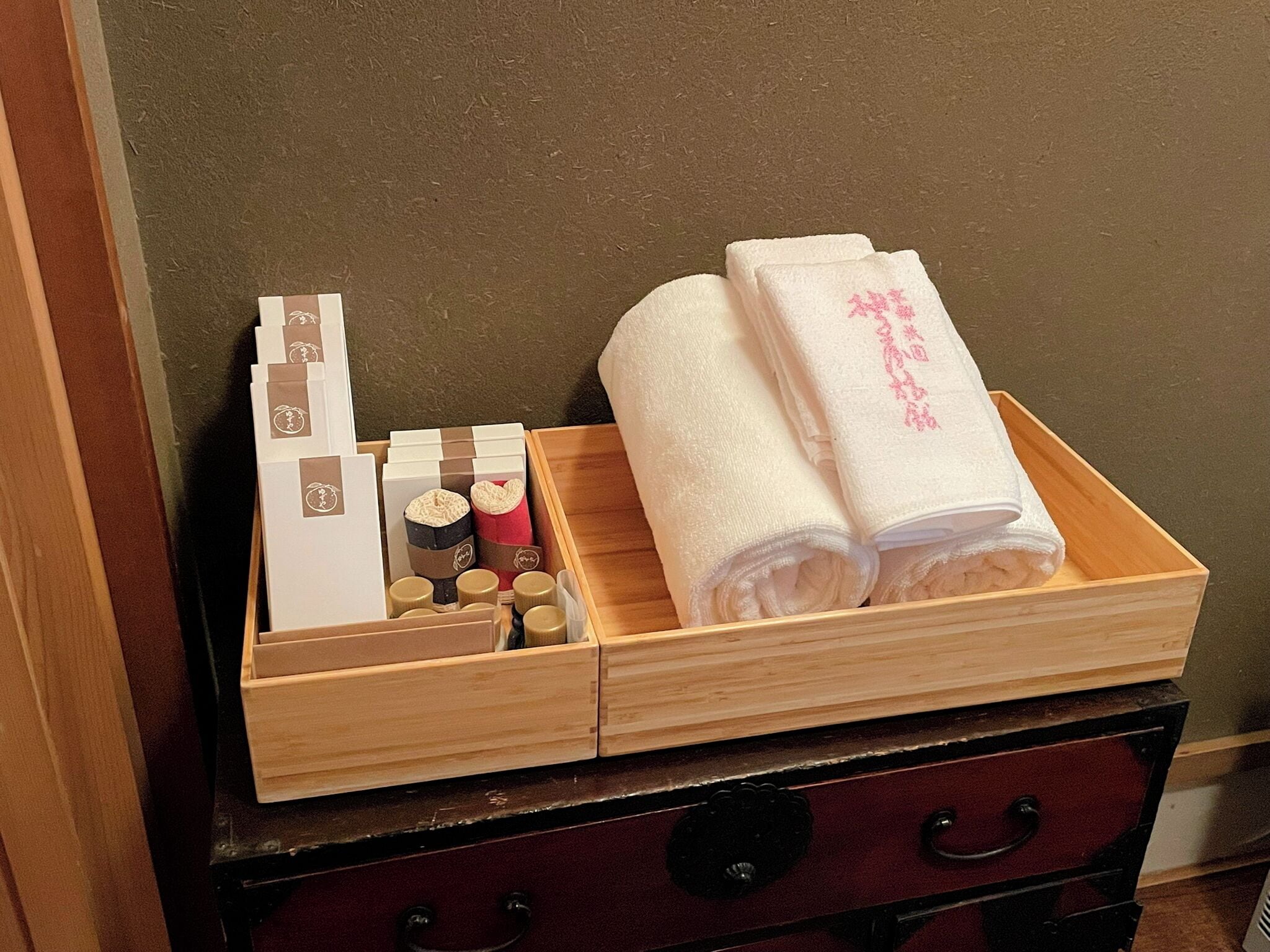 A wooden chest with compartments containing folded towels, bottles, and packaged items.