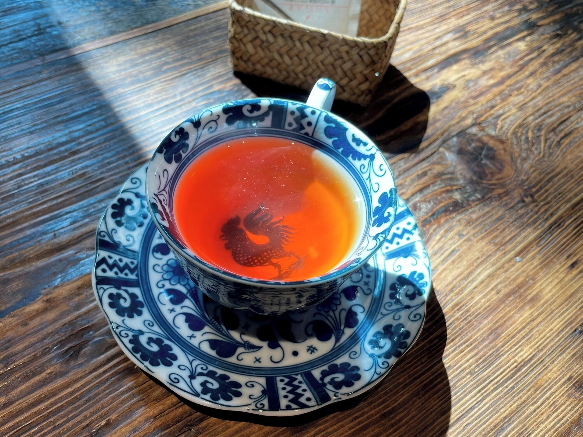 A cup of tea on a patterned saucer and plate, placed on a wooden table.