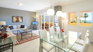 En moderne stue med et glasbord, hvide sofaer og et fjernsyn.
