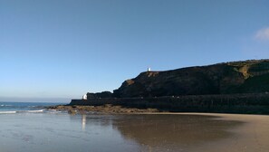 A coastal scene with a lighthouse on a cliff, a sandy beach, and the ocean.