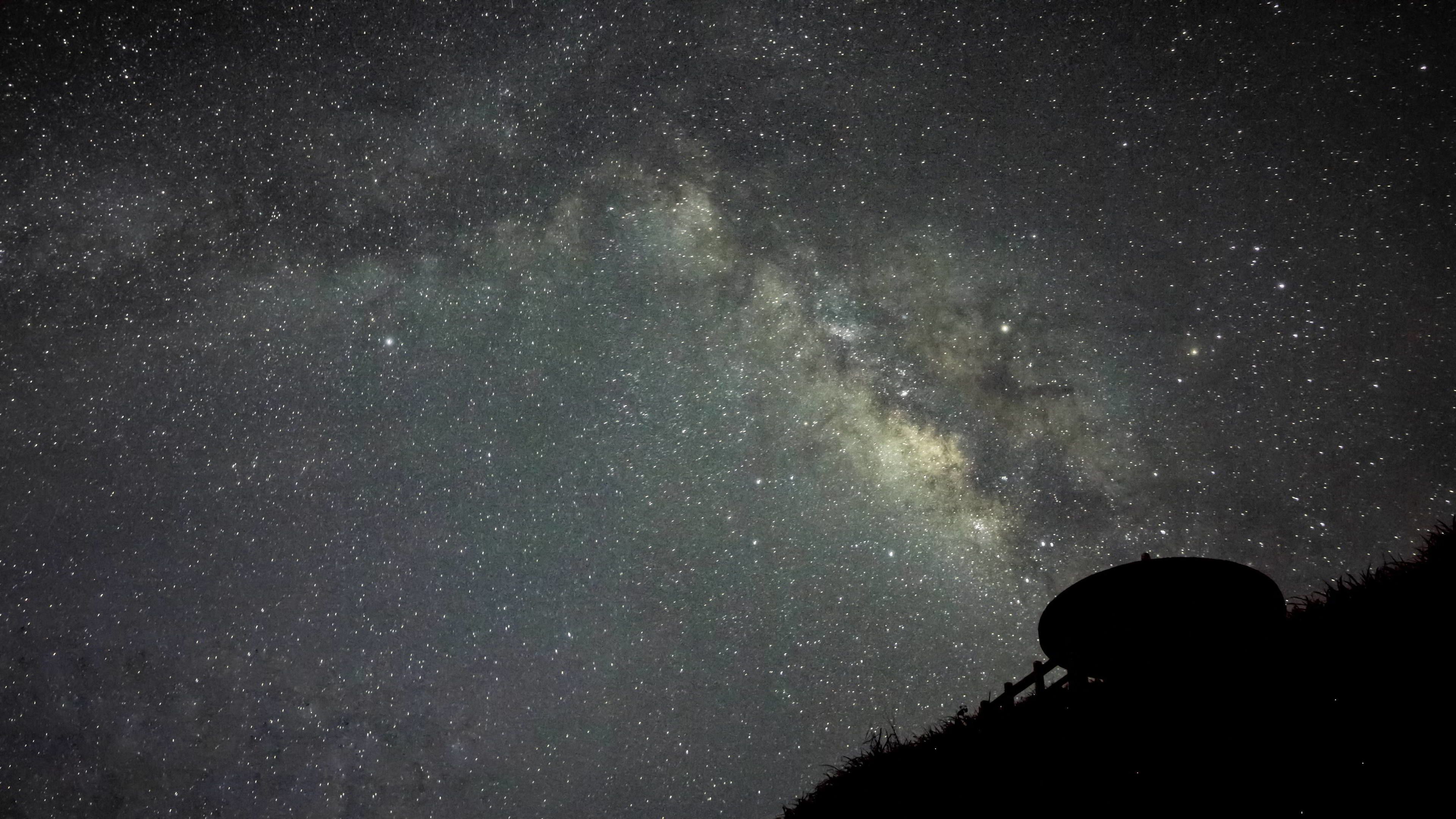 A night sky filled with stars and the Milky Way, viewed from a hilltop with a telescope.