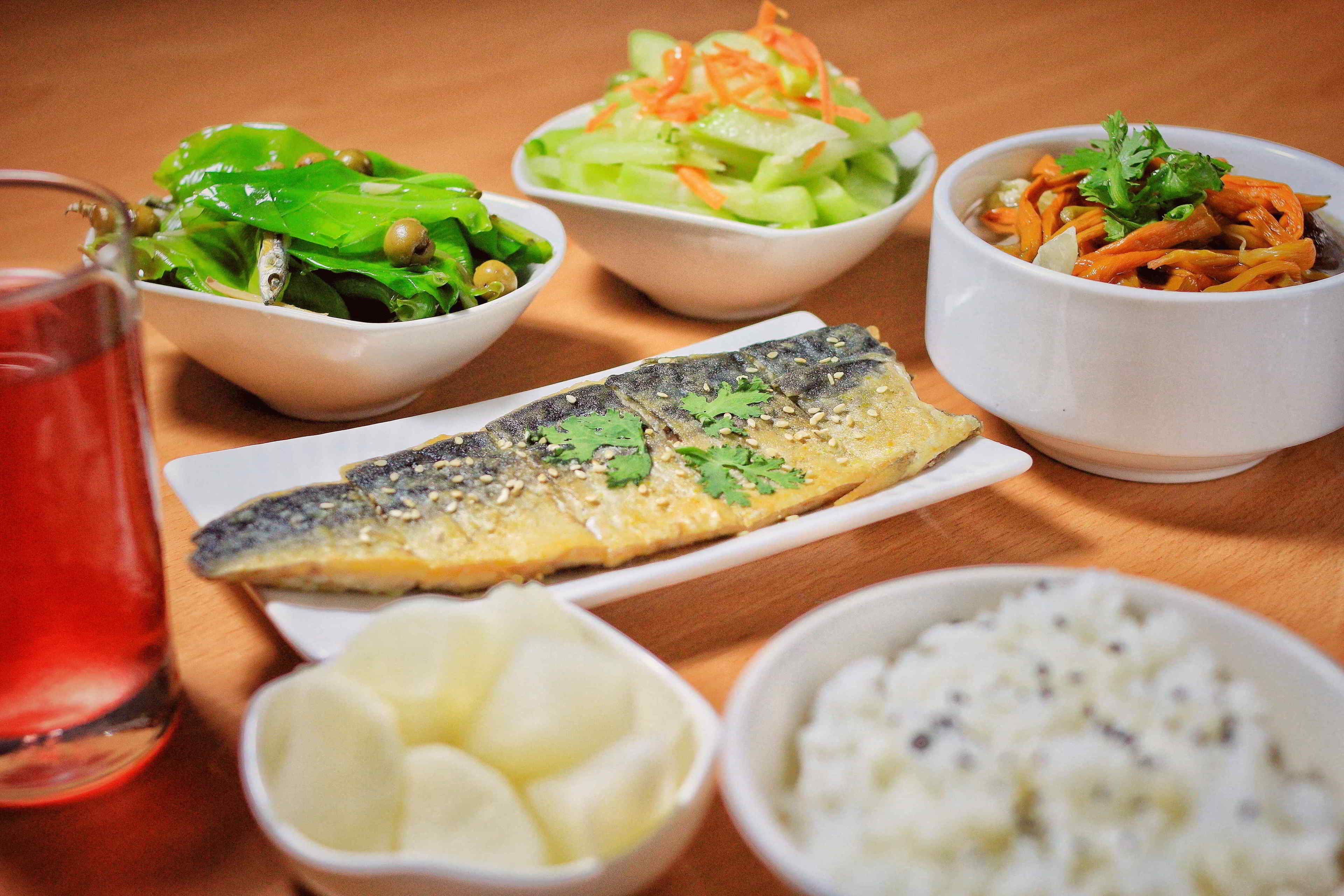 Un tavolo con diversi piatti, tra cui pesce, insalata e riso.
