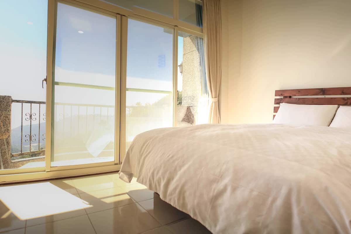 A bedroom with a large bed, a wooden headboard, and a sliding glass door leading to a balcony.