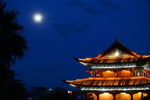 A traditional multi-tiered building with illuminated rooftops and red lanterns, set against a night sky with a visible moon. - Dali Yun Xi Boutique Inn (Dali)