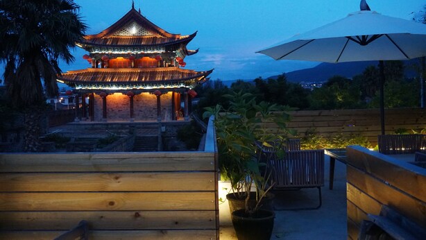 A traditional multi-tiered building with illuminated lanterns, a wooden bench, and an umbrella. - Dali Yun Xi Boutique Inn (Dali)