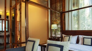 A room with a wooden ceiling, a bed with white bedding and blue pillows, a chair with a cushion, a nightstand with a lamp, and a window with blinds. - Dali Yun Xi Boutique Inn (Dali)