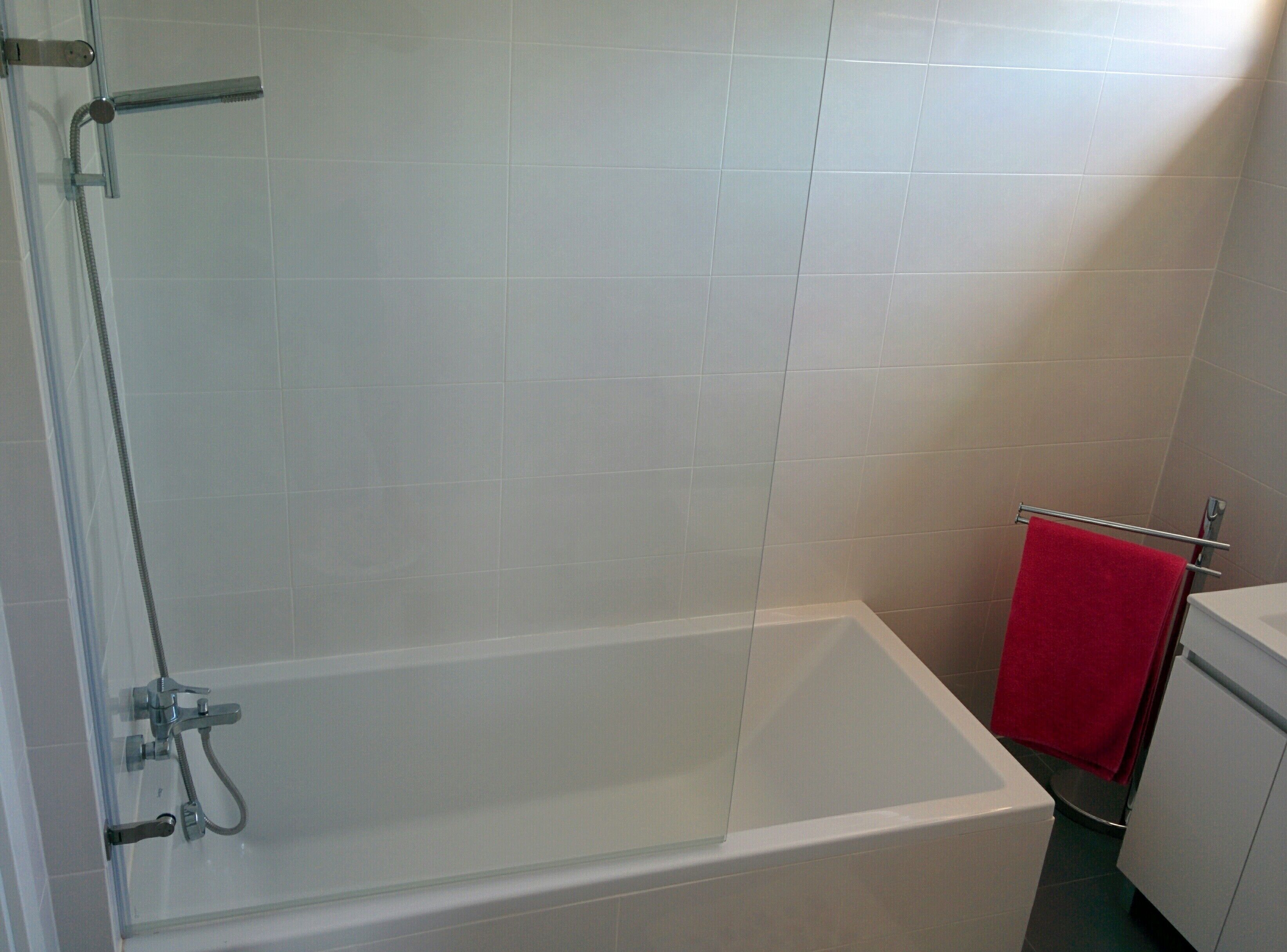 Ein Badezimmer mit einer gläsernen Duschkabine, einer weißen Badewanne und einem roten Handtuch an einem Halter.