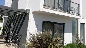 A modern two-story building with a balcony, large windows, and a covered entrance area with bicycles.