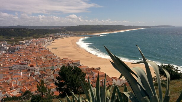 A coastal town with terracotta-roofed buildings, a sandy beach, and a view of the ocean.