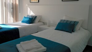 A hotel room with two beds, each with a blue and white bedspread, and a white headboard. There are two framed pictures on the wall, one of a bus and one of a bicycle.