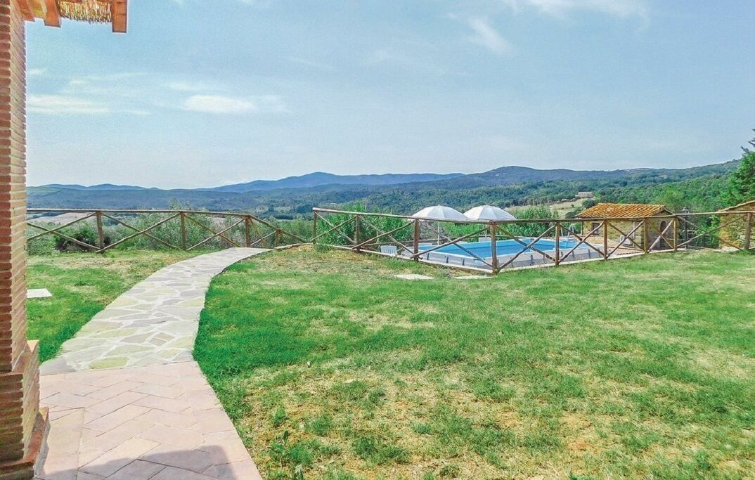 Un espace piscine avec un chemin de pierre menant à une pelouse, entouré de structures en bois et offrant une vue sur des collines lointaines.