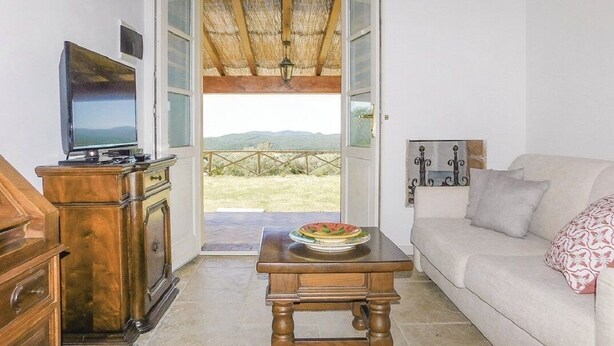 A living room with a TV, wooden furniture, a sofa, and a view of the outdoors. - Tuscany: House "Old Abbey" among the olive trees with pool (Monteverdi Marittimo - PI -)