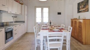 A dining area with a table set for six, white chairs, a wooden cabinet, and a window with natural light. - Tuscany: House "Old Abbey" among the olive trees with pool (Monteverdi Marittimo - PI -)