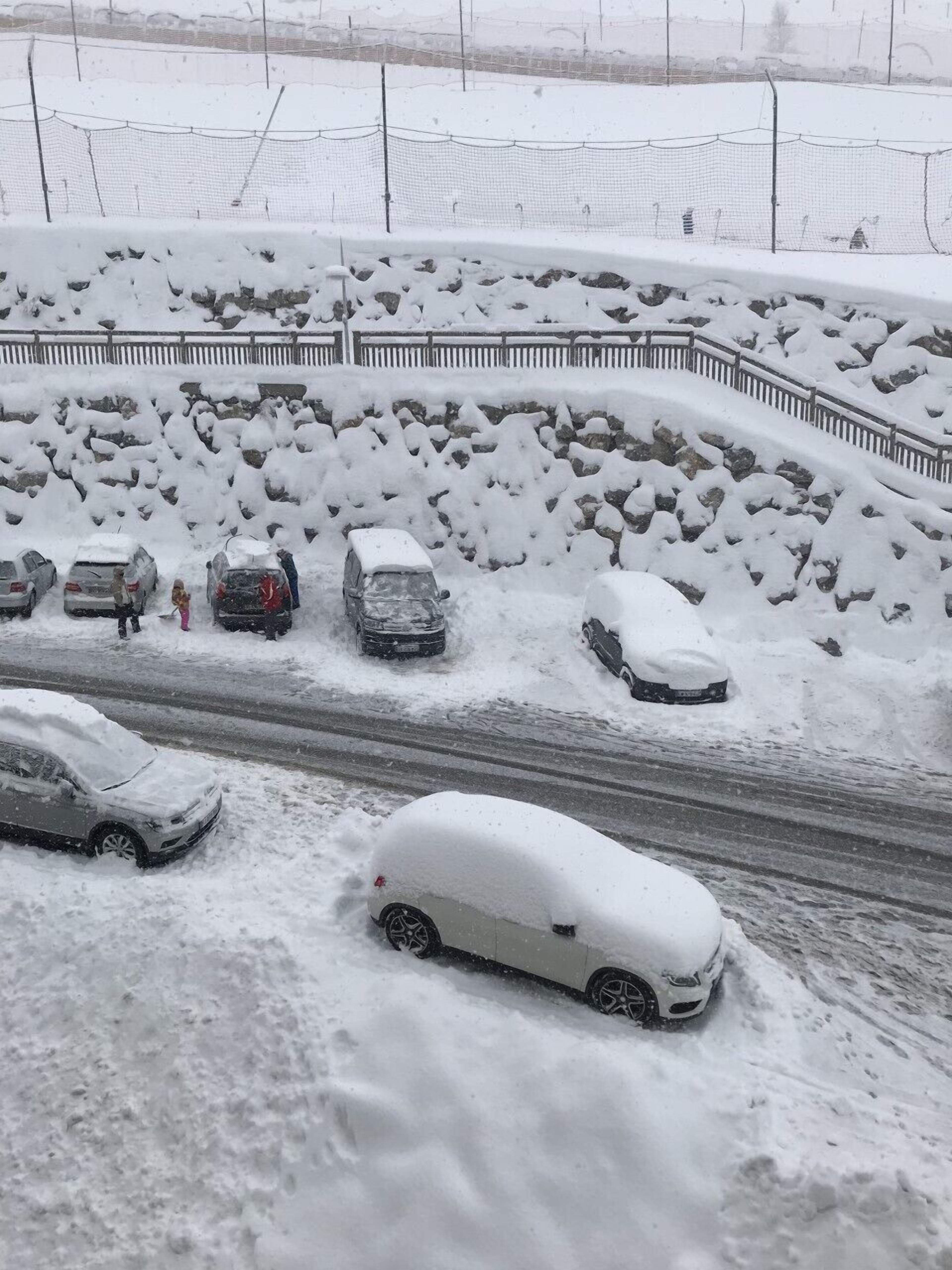Un parking enneigé où plusieurs voitures sont recouvertes de neige.