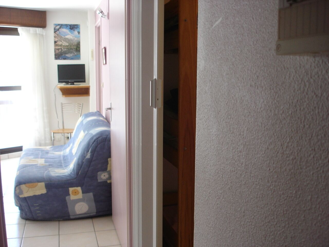 Une pièce avec un canapé bleu, un téléviseur posé sur un meuble et un tableau accroché au mur.
