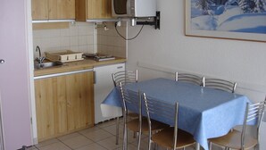 A compact kitchen with wooden cabinets, a microwave, a sink, and a dining table with chairs.