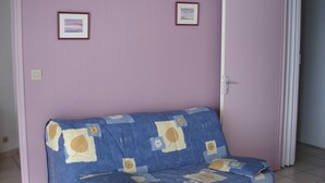 A room with a blue sofa against a pink wall, two framed pictures, and a door leading to another room.