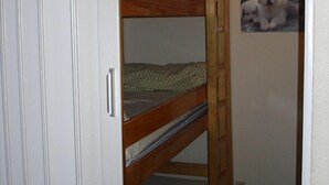 A bunk bed room with a wooden ladder, a small bed at the bottom, and a larger bed at the top. There is a wall-mounted light and a framed picture of dogs.