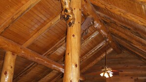 Ein Blockhaushaus-Interieur mit Holzbalkendecke, großen Fenstern und einem Bett mit Decken.