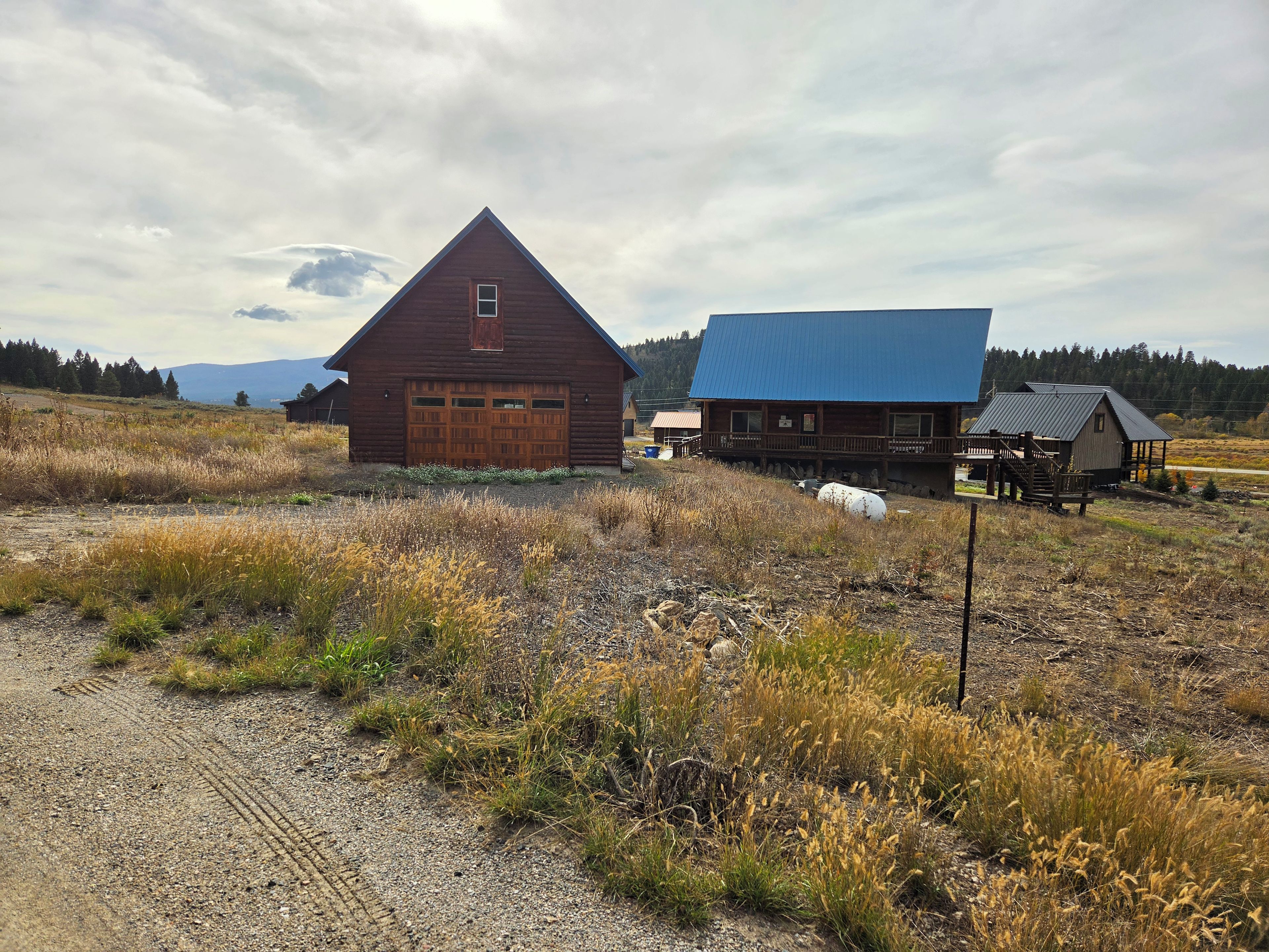 A rural landscape with a large wooden barn and a smaller building with a blue roof.