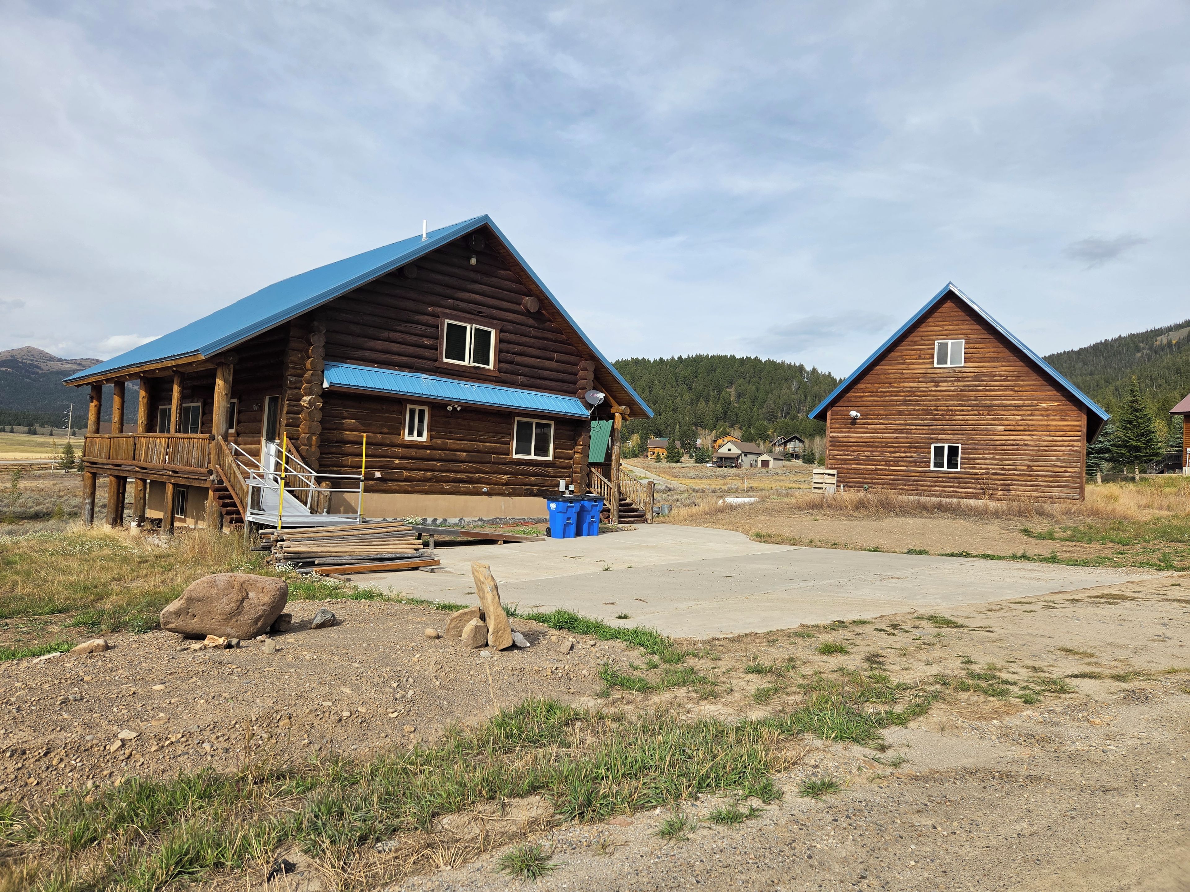 A rustic wooden cabin with a blue roof, a porch, and a visible staircase.