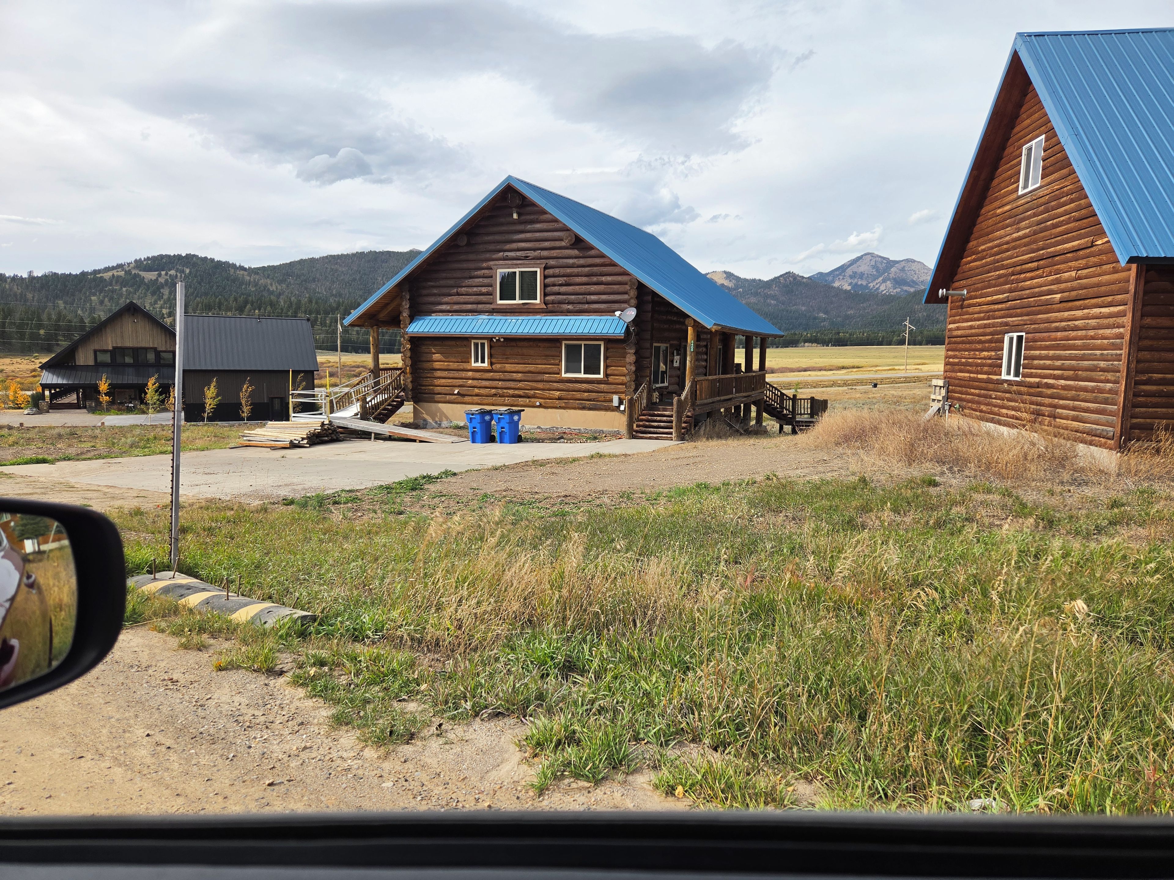 A wooden cabin with a blue roof, a porch, and a dirt driveway.