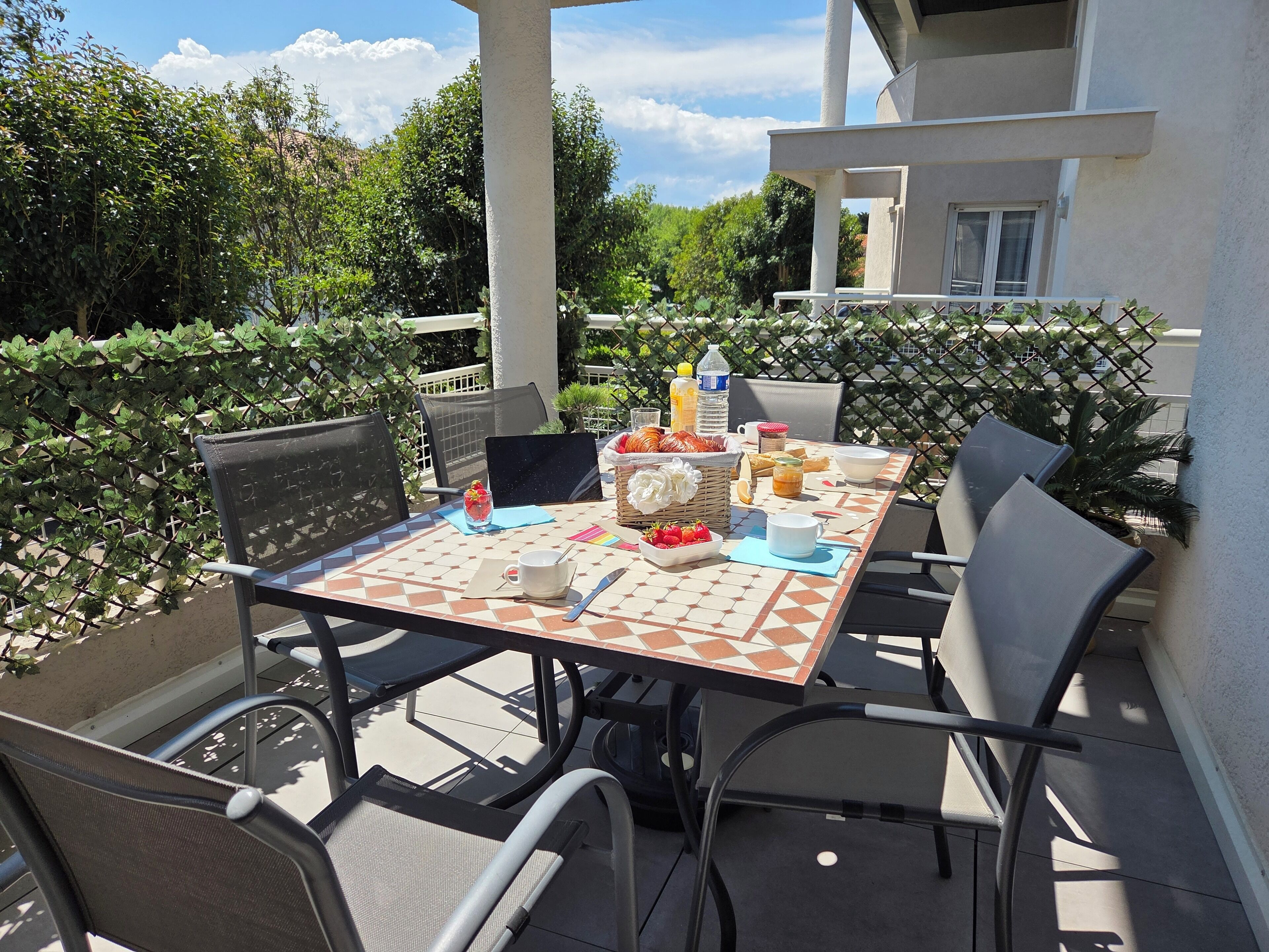 Un espace extérieur aménagé pour les repas, avec une table dressée pour quatre personnes, entourée de chaises.