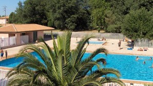 A swimming pool with people around it, surrounded by palm trees and a fenced area. - Grand T3 60 m², pool, 2 parking, 4 bikes, Beach, Shops, Marina Port (Saint-Cyprien)