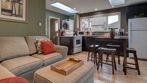Un appartement moderne comprenant un salon, une cuisine et un coin repas. Il est équipé d’un canapé, d’un pouf et d’une table basse en bois.